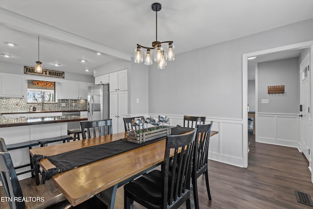 dining area with visible vents, dark wood-type flooring, wainscoting, a decorative wall, and a notable chandelier