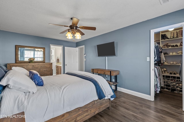 bedroom featuring a textured ceiling, wood finished floors, a closet, baseboards, and a spacious closet