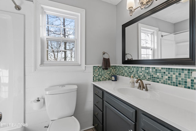 bathroom with walk in shower, toilet, vanity, wainscoting, and tile walls