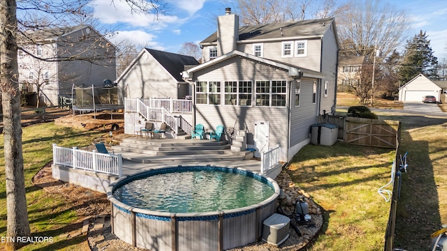 rear view of house featuring a gate, fence, a wooden deck, a trampoline, and a lawn