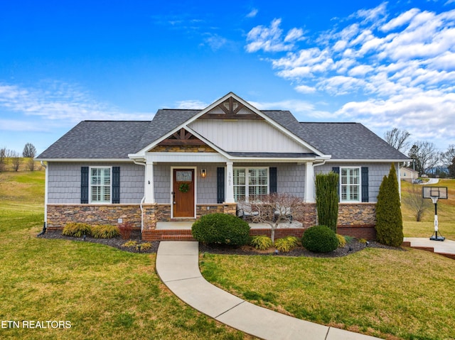 craftsman-style home with a front lawn, covered porch, stone siding, and a shingled roof