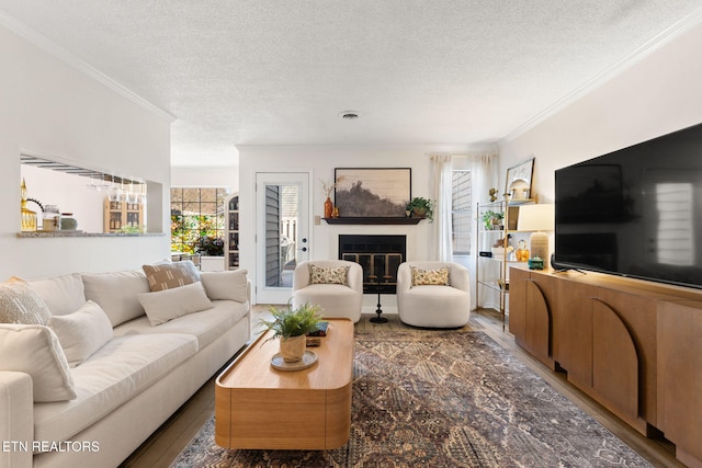 living area featuring a glass covered fireplace, ornamental molding, a textured ceiling, and wood finished floors