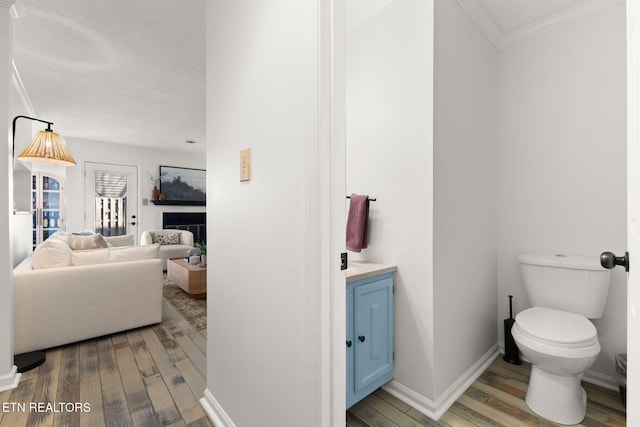 bathroom with vanity, wood finished floors, baseboards, crown molding, and toilet