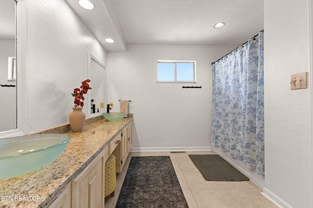 bathroom with baseboards, double vanity, a sink, a textured ceiling, and tile patterned floors