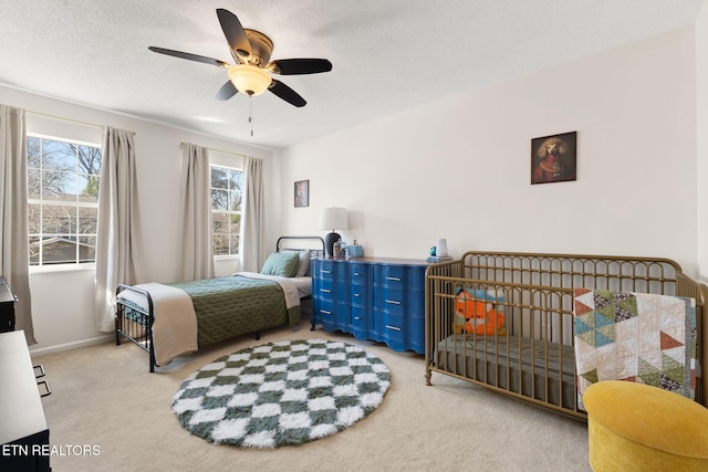 bedroom featuring baseboards, light colored carpet, a ceiling fan, and a textured ceiling