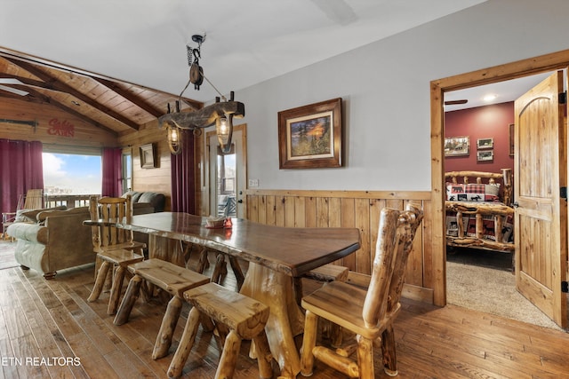 dining room with hardwood / wood-style floors, wooden ceiling, wainscoting, wood walls, and vaulted ceiling