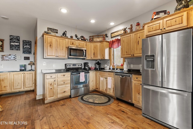 kitchen with dark countertops, appliances with stainless steel finishes, light brown cabinetry, and hardwood / wood-style flooring