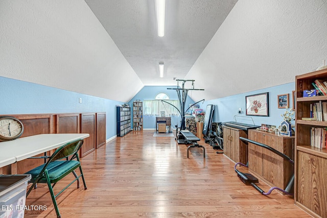 exercise room with baseboards, a textured ceiling, lofted ceiling, and light wood-style floors