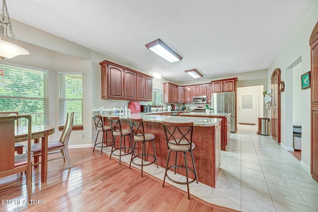 kitchen featuring baseboards, light wood-style flooring, a kitchen breakfast bar, appliances with stainless steel finishes, and a peninsula