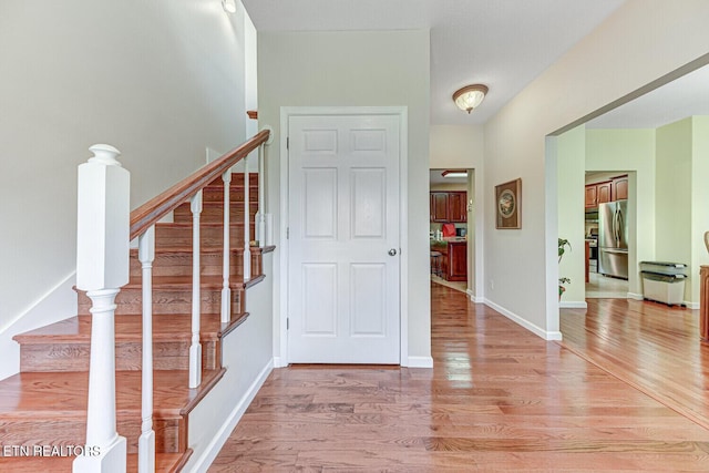 foyer entrance featuring light wood finished floors, stairway, and baseboards