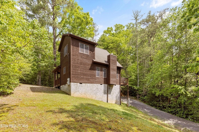 view of home's exterior featuring a forest view, roof with shingles, a yard, a chimney, and crawl space