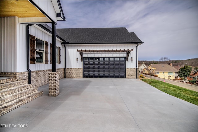 view of side of home with brick siding, concrete driveway, a garage, and roof with shingles