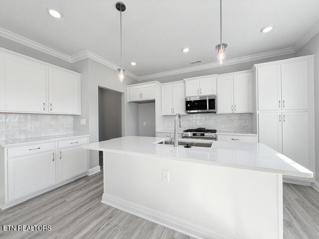 kitchen with a large island, a sink, stainless steel microwave, white cabinets, and light wood finished floors