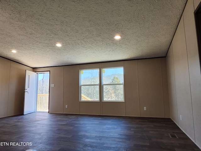 spare room with a decorative wall, dark wood-style floors, visible vents, and a textured ceiling