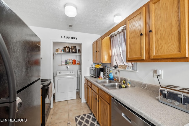 kitchen featuring light tile patterned flooring, a sink, light countertops, appliances with stainless steel finishes, and washing machine and dryer