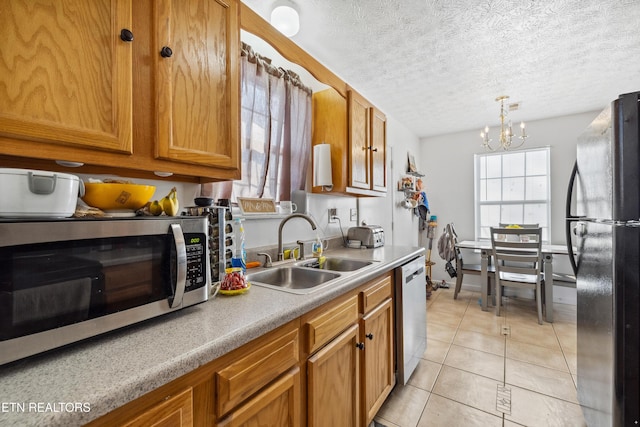 kitchen with a sink, appliances with stainless steel finishes, light tile patterned flooring, brown cabinetry, and a chandelier