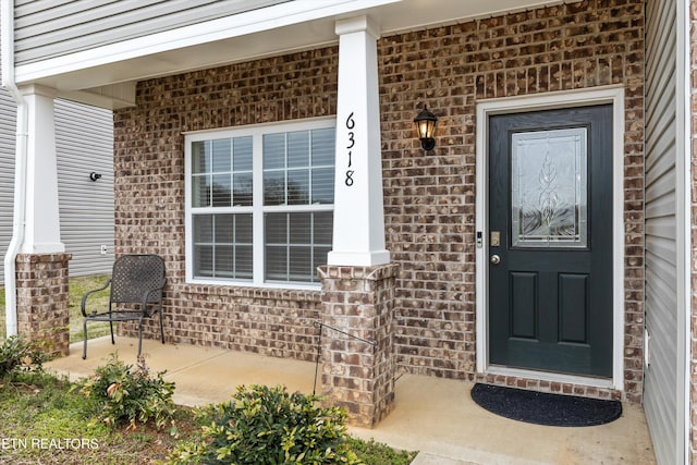 doorway to property featuring brick siding and a porch