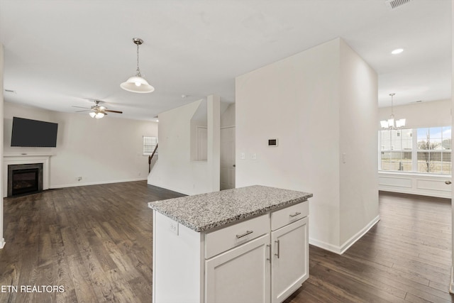 kitchen featuring hanging light fixtures, light stone counters, dark wood-style floors, and a fireplace