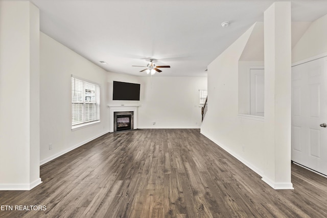 unfurnished living room with ceiling fan, baseboards, dark wood-style floors, and a high end fireplace