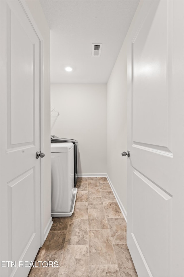 clothes washing area with visible vents, stone finish flooring, baseboards, washing machine and dryer, and laundry area