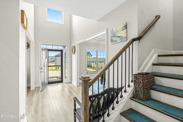 foyer featuring baseboards, a high ceiling, wood finished floors, and stairs