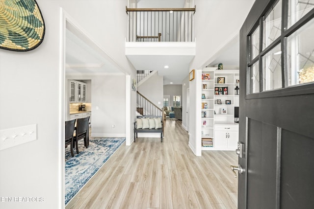 entrance foyer featuring crown molding, baseboards, stairs, and light wood-style floors