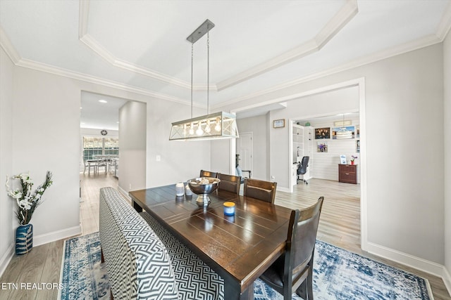 dining room featuring a tray ceiling, baseboards, wood finished floors, and ornamental molding