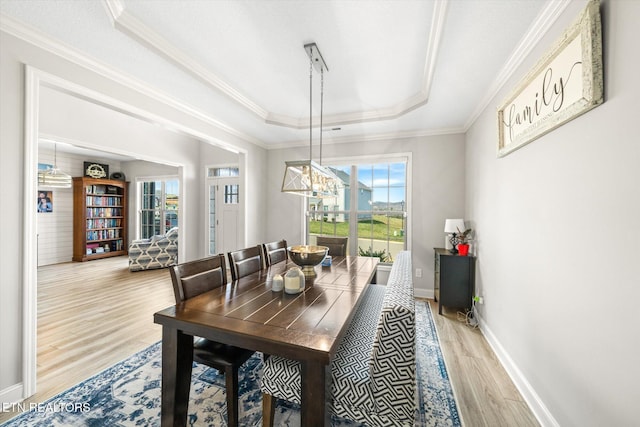 dining area featuring crown molding, a raised ceiling, baseboards, and wood finished floors