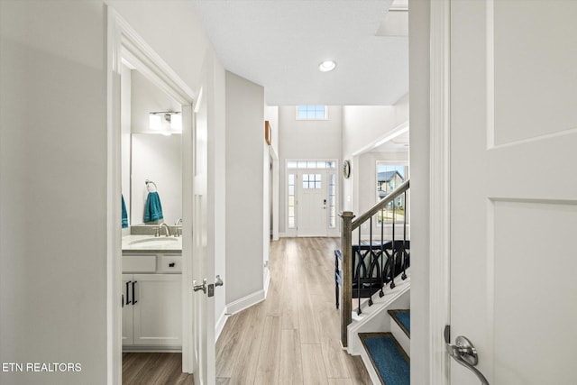 hallway featuring a sink, recessed lighting, light wood finished floors, baseboards, and stairs