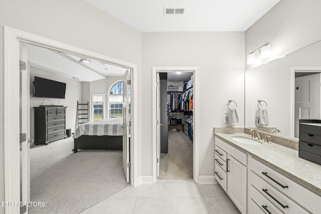 bathroom with tile patterned flooring, visible vents, a walk in closet, baseboards, and vanity