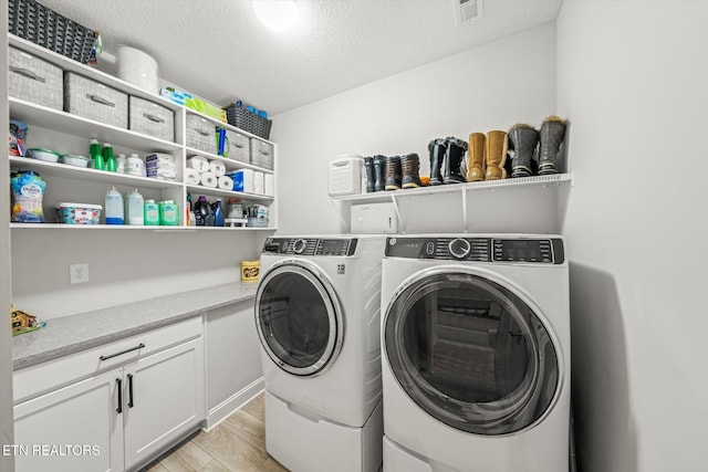 laundry room featuring washer and clothes dryer, visible vents, light wood finished floors, and a textured ceiling