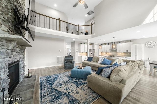 living room with a stone fireplace, light wood-style flooring, a ceiling fan, and visible vents