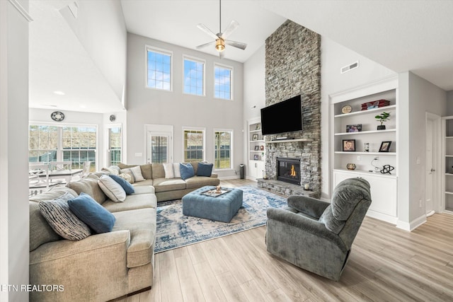 living room with visible vents, built in shelves, baseboards, a stone fireplace, and light wood-style flooring