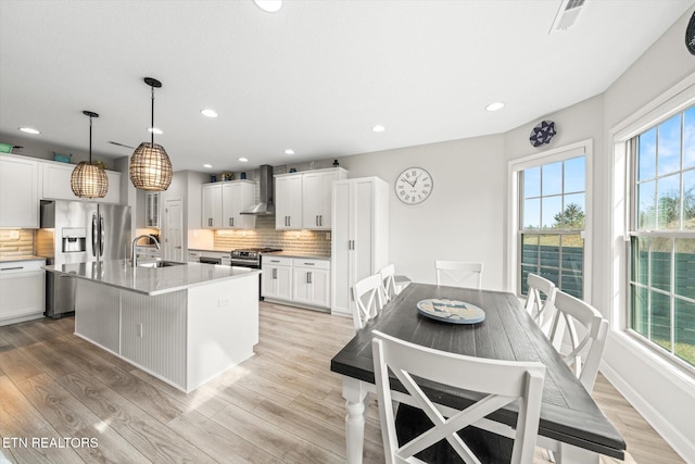 kitchen with decorative backsplash, light wood-type flooring, wall chimney range hood, and a sink