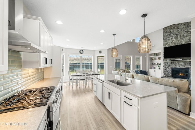 kitchen with light wood-style flooring, a sink, white cabinetry, appliances with stainless steel finishes, and wall chimney range hood