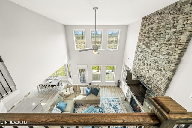 living area with a high ceiling, a stone fireplace, wood finished floors, and a healthy amount of sunlight