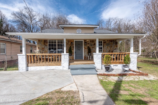 view of front of house featuring stone siding, roof with shingles, a porch, and fence