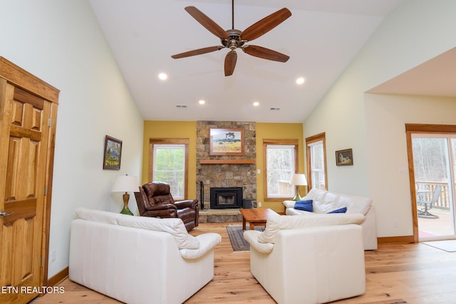 living room with a stone fireplace, light wood-style flooring, high vaulted ceiling, and baseboards