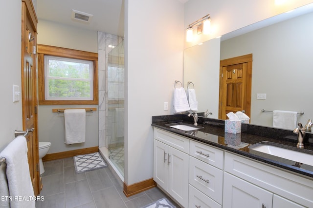 bathroom with a sink, toilet, double vanity, and a tile shower