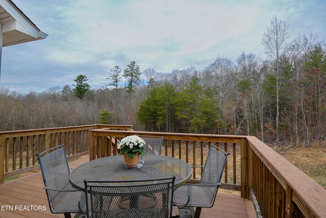 wooden terrace with a wooded view and outdoor dining area