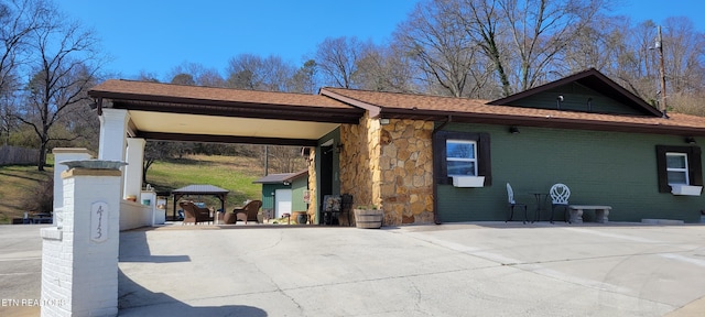 view of side of property with a gazebo, stone siding, and concrete driveway