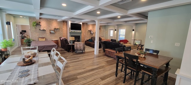 dining area featuring visible vents, decorative columns, a fireplace, wood finished floors, and coffered ceiling