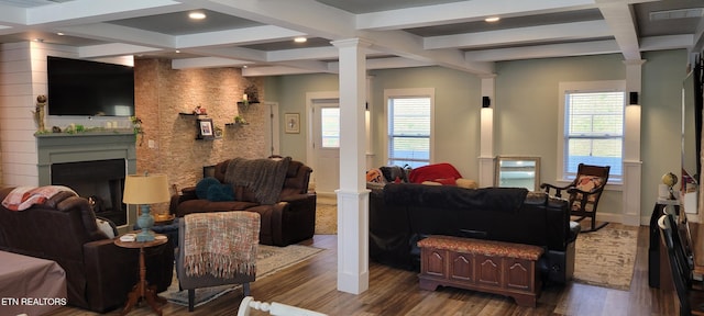 living room featuring beam ceiling, coffered ceiling, wood finished floors, a fireplace, and ornate columns