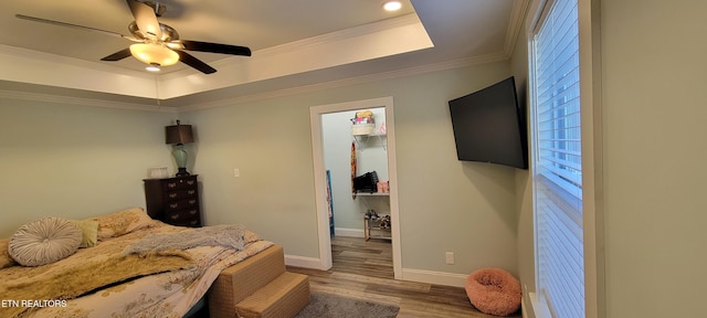 bedroom with wood finished floors, baseboards, ceiling fan, crown molding, and a raised ceiling