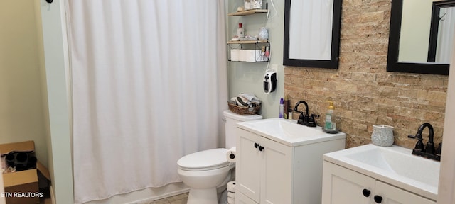 bathroom with brick wall, toilet, and vanity