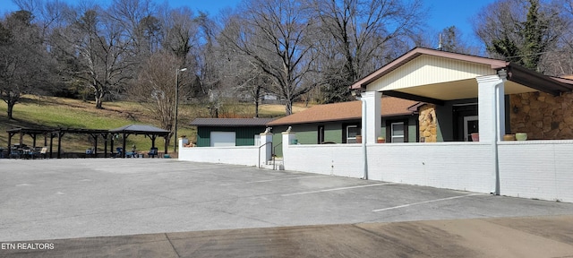 view of home's exterior with a gazebo, a fenced front yard, stone siding, and uncovered parking