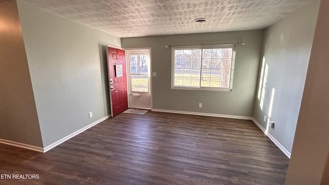 foyer entrance featuring visible vents, a textured ceiling, dark wood-type flooring, and baseboards