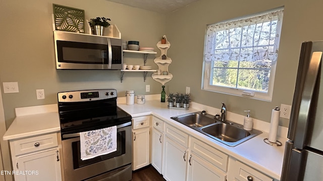 kitchen featuring appliances with stainless steel finishes, white cabinetry, light countertops, and a sink