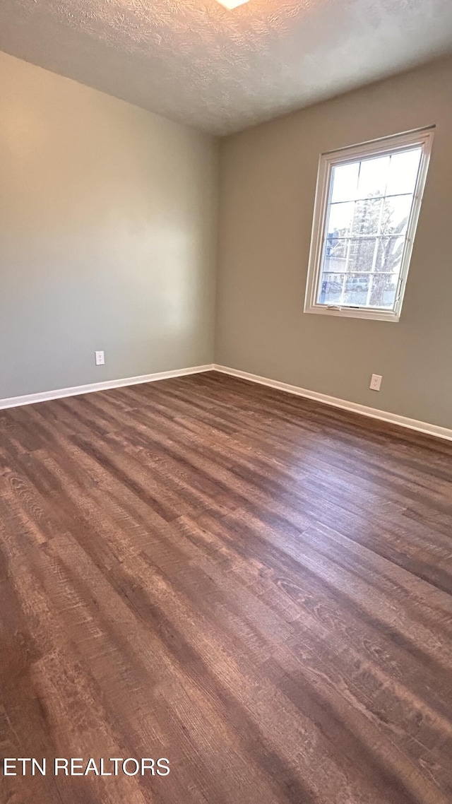 empty room with baseboards, a textured ceiling, and dark wood-style flooring