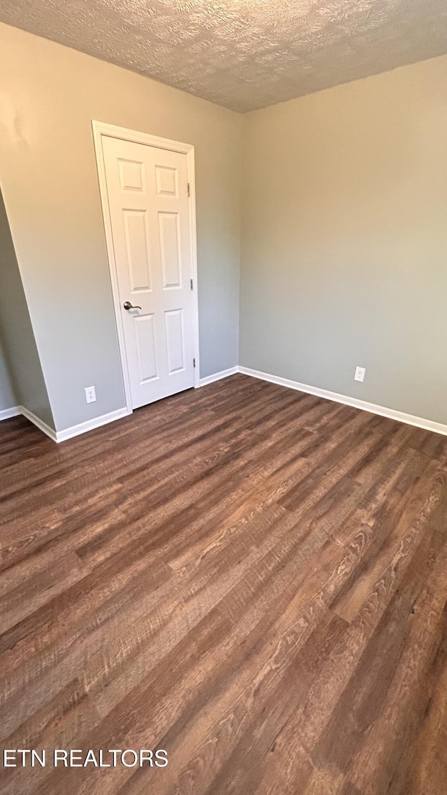 empty room with a textured ceiling, baseboards, and dark wood-style flooring